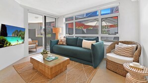 A modern living room with a sofa, a coffee table, and a wicker chair. - Seaside Getaway Large Private Courtyard - Parking (Surfers Paradise)