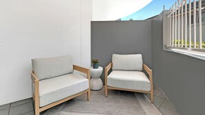 A small, enclosed balcony with two wooden chairs and a round table, featuring a grey wall and a white railing. - Seaside Getaway Large Private Courtyard - Parking (Surfers Paradise)