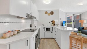 A modern kitchen with white cabinetry, a built-in microwave, and a stove. - Seaside Getaway Large Private Courtyard - Parking (Surfers Paradise)