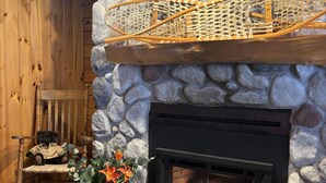 A stone fireplace with a fire, a wooden bench, a teddy bear, and a bear statue. - Allen Falls Private Woodland Cabin on 30 acres (Potsdam)