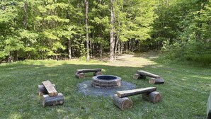 A circular fire pit surrounded by logs in a grassy area with trees in the background. - Allen Falls Private Woodland Cabin on 30 acres (Potsdam)