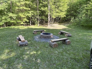 A circular fire pit surrounded by logs in a grassy outdoor area with trees in the background. - Allen Falls Private Woodland Cabin on 30 acres (Potsdam)