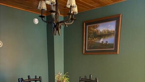 A dining area with a round wooden table surrounded by chairs, a chandelier, a framed landscape painting, and a patterned rug. - Allen Falls Private Woodland Cabin on 30 acres (Potsdam)