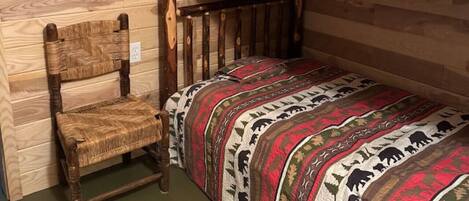 Un letto a castello con una coperta fantasia, una sedia di legno e una parete in legno.