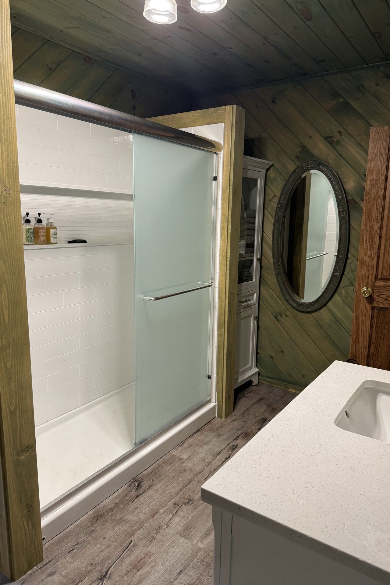 A bathroom with a glass-enclosed shower, a wooden vanity, and a round mirror.