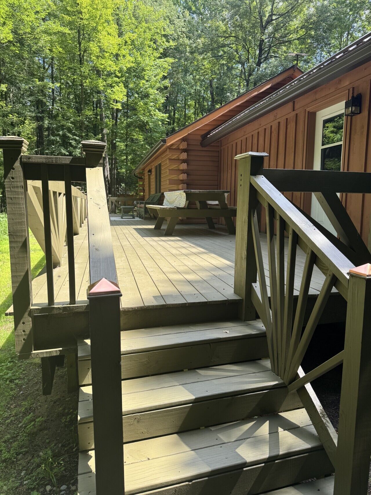 A wooden deck leading to a cabin with a picnic table and a bench.
