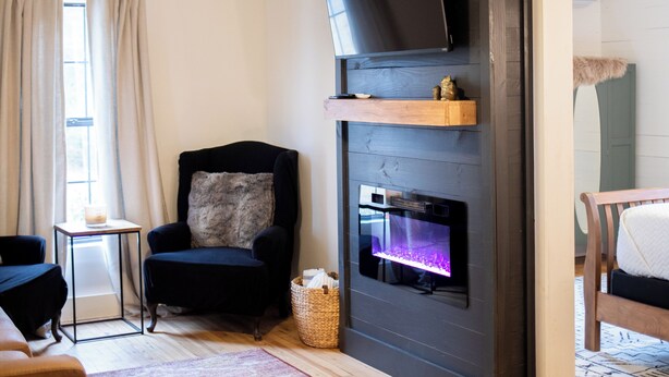 A modern living room with a fireplace, a ceiling fan, a flat-screen TV, and a comfortable seating area. - One Eyed Odie's Cozy 3-bed, 1-bath home with a relaxing hot tub. (Cove)