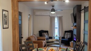 A dining area with a round wooden table, dark chairs, and a modern light fixture above. - One Eyed Odie's Cozy 3-bed, 1-bath home with a relaxing hot tub. (Cove)