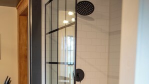 A modern shower with glass doors and a tiled wall. - One Eyed Odie's Cozy 3-bed, 1-bath home with a relaxing hot tub. (Cove)