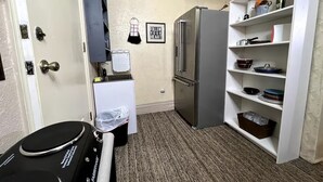 A compact kitchen with a refrigerator, a microwave, and a sink. There is a wall-mounted rack with dishes and a small shelf with kitchenware. A door with a doorknob and a towel hanging on it is visible. - Private and cozy stay 2-bedroom apartment with AC in Oklahoma City (Oklahoma City)