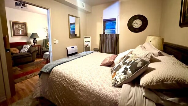 A hotel room with a large bed, a desk, a chair, a lamp, a clock, and a window with blinds. - Private and cozy stay 2-bedroom apartment with AC in Oklahoma City (Oklahoma City)