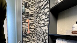 A shower with a glass door, a tiled wall, and a shelf with a book and a towel. - Private and cozy stay 2-bedroom apartment with AC in Oklahoma City (Oklahoma City)