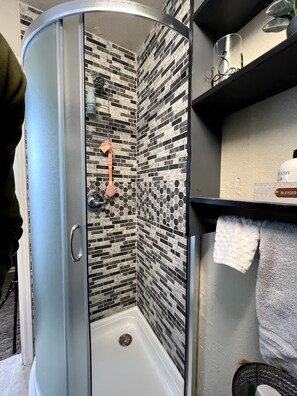 A shower with a glass door, a tiled wall, and a shelf with a book and a towel. - Private and cozy stay 2-bedroom apartment with AC in Oklahoma City (Oklahoma City)