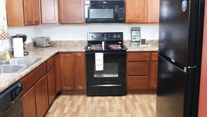 A kitchen with wooden cabinets, a black microwave, a stove, a refrigerator, and a dishwasher.