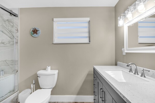 A bathroom with a toilet, a sink, a vanity, a shower, and a mirror with lights. - CANAL FRONT HOME OCEAN ACCESSIBLE (Marathon)