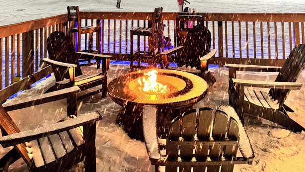Ein mit Schnee bedeckter Deck mit Sitzgelegenheiten im Freien und einer Feuerstelle.
