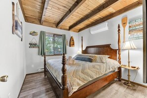 A bedroom with a wooden bed, a window with curtains, a wall-mounted air conditioner, and a wall with motivational quotes.