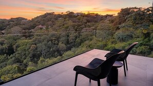 Terraza con dos sillas y una mesa, con vistas a un paisaje boscoso al atardecer.