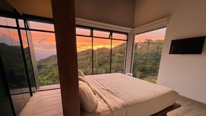 Een slaapkamer met een groot raam dat uitzicht biedt op een glooiend landschap.