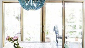 Un espace repas comprenant une table, des chaises, un lustre et une vue dégagée grâce à de grandes portes vitrées.