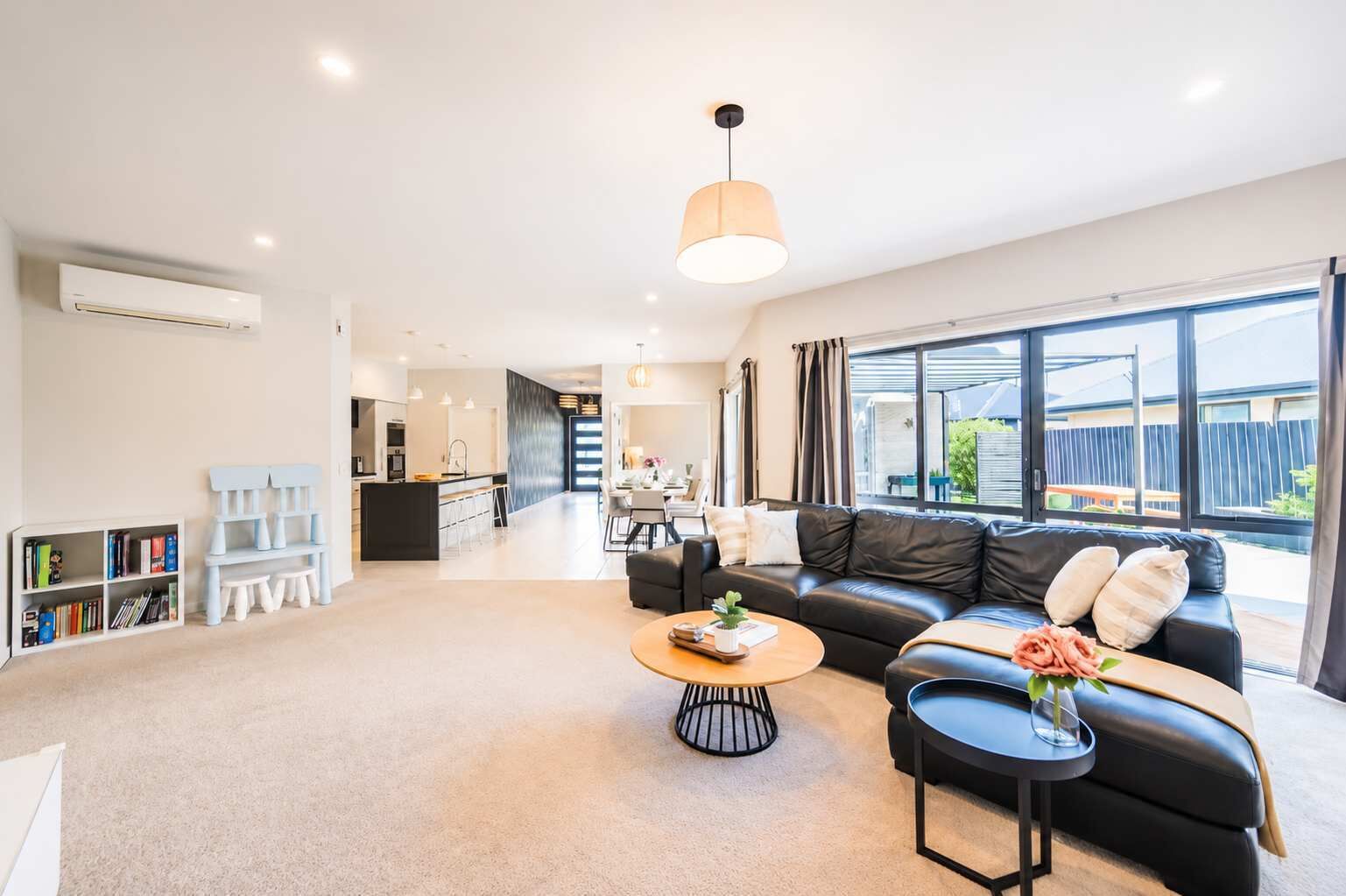 A modern living room with a black leather sofa, a coffee table, and a bookshelf.