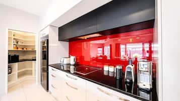 Una cocina moderna con encimera negra, armarios blancos y salpicadero rojo.