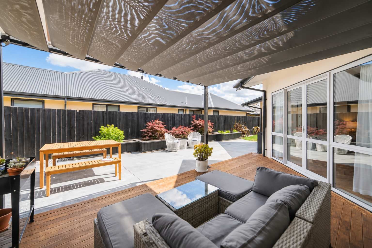 A covered patio with a wooden table, a sofa, and potted plants.