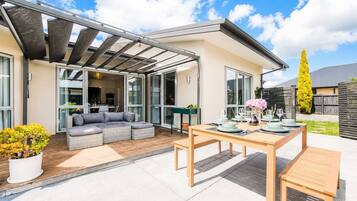 Moderni patio, jossa on neljälle henkilölle katettu ruokapöytä, harmaa sohva ja pergola.