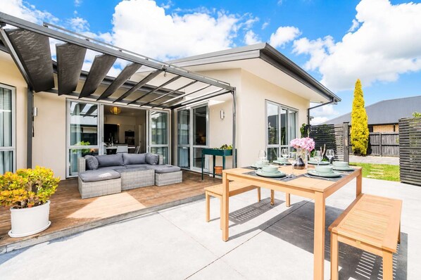 A modern patio with a dining table set for four, a grey sofa, and a pergola structure.