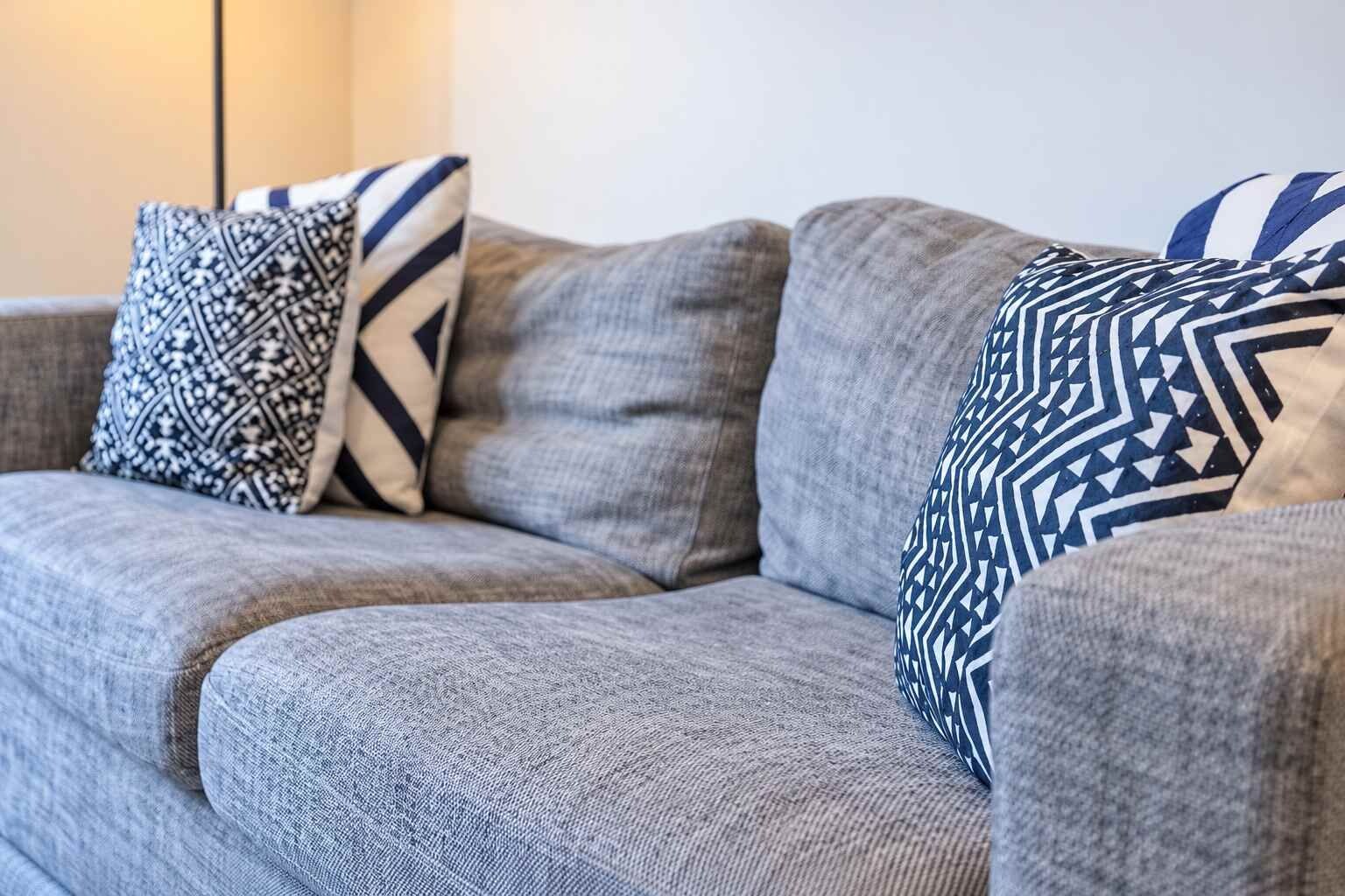 Een grijze bank met gekleurde kussens in een kamer met een neutrale kleurstelling.
