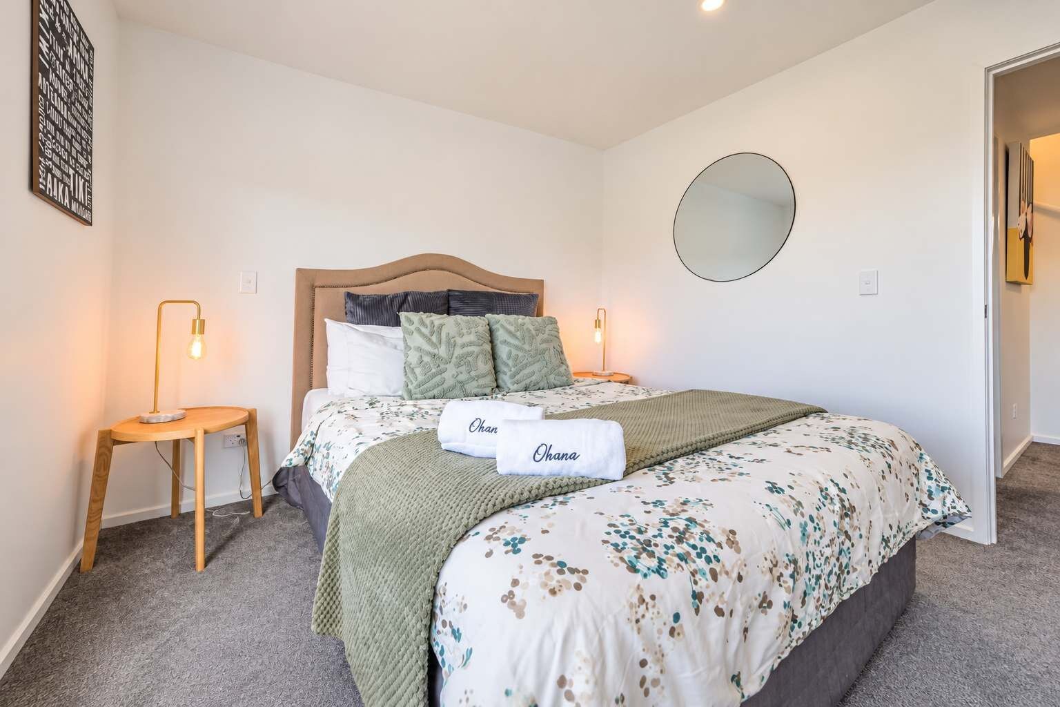 Un dormitorio con una cama, dos lámparas de noche, un espejo redondo y una pequeña mesa de madera.