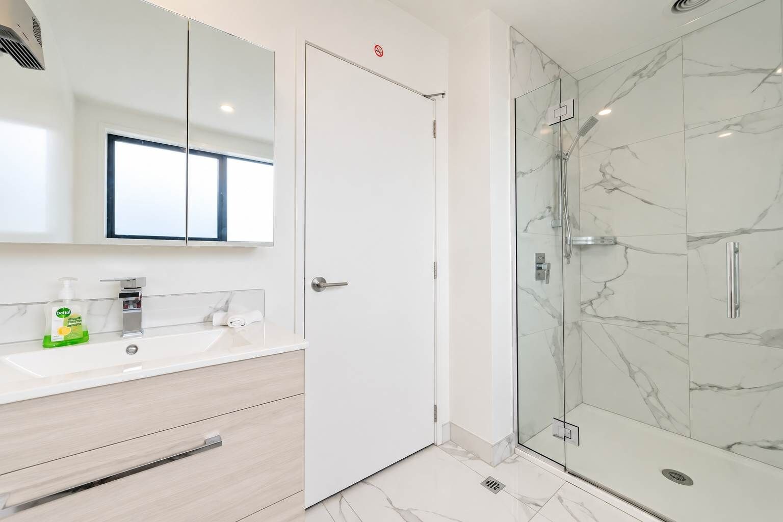 A modern bathroom with a glass-enclosed shower, a white vanity with a mirror, and a bottle of hand soap.