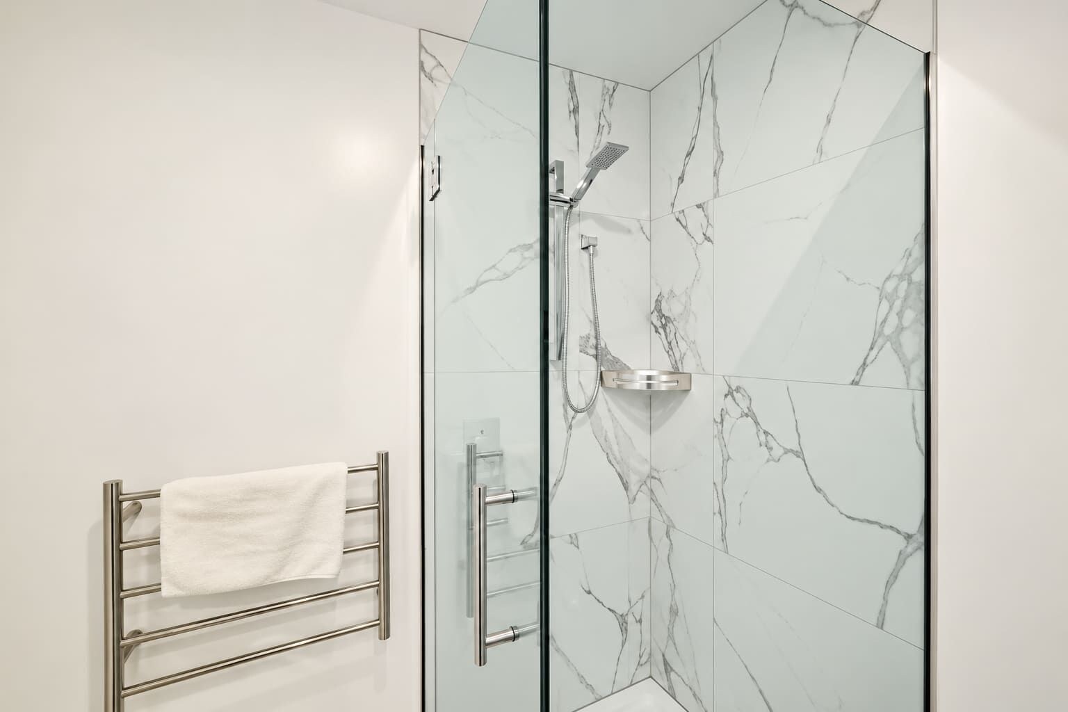 A glass-enclosed shower with a handheld showerhead and a handheld shower attachment.