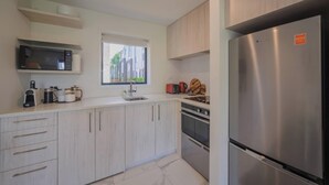 Una cocina moderna con armarios de madera clara, un refrigerador de acero inoxidable, un microondas, una cafetera y un ventanal con vistas al exterior.