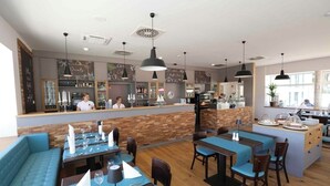 En restaurang med trägolv, blå stoppade sittplatser och en bardisk.