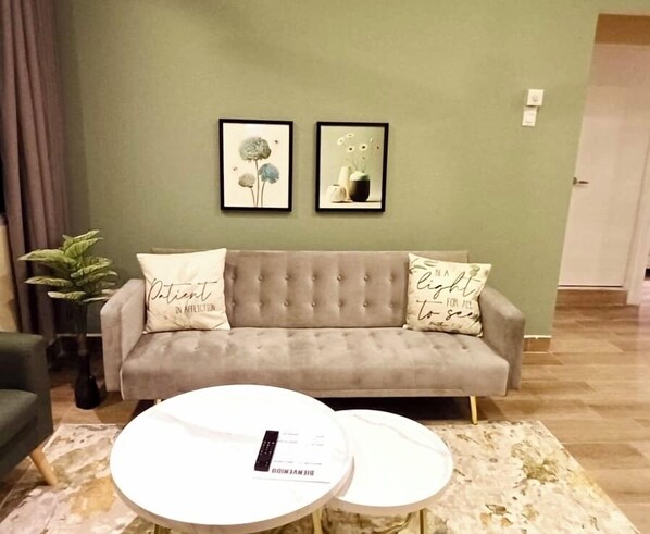 Ein Wohnzimmer mit einem grauen Sofa, zwei runden weißen Couchtischen und zwei gerahmten Bildern an der Wand.