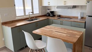 A modern kitchen with a wooden countertop, two white chairs, and light green cabinets.