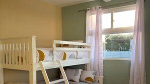 A bunk bed room with a window, curtains, and a tiled floor.