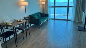 Una habitación con un sofá verde, una mesa de comedor con sillas y un ventanal con vistas al mar.