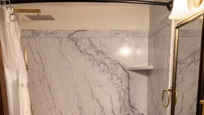 Un baño con pared de ducha de mármol, un lavamanos blanco y un mueble de tocador de madera.