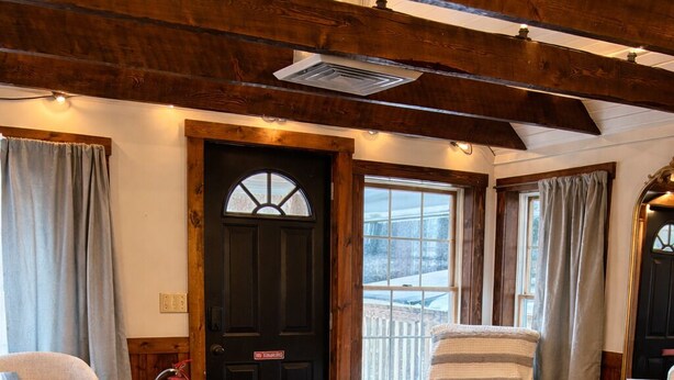 Una habitación acogedora con suelo de madera, una puerta negra, un sillón blanco y una mesita de noche con una lámpara.