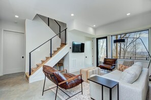 A modern living room with a staircase, leather armchair, sofa, and a flat-screen TV. - Modern Mountain Sanctuary on 37 Private Acres; Views, Trails, Hot Tub,Workspaces (Black Mountain)