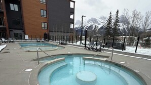 Et poolområde med to runde pools, omgivet af liggestole og udsigt til bjerge.