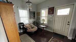 Un salon doté d’un parquet en bois foncé, d’un fauteuil beige, d’une petite table ronde avec une lampe, d’une machine à café et d’un tapis.