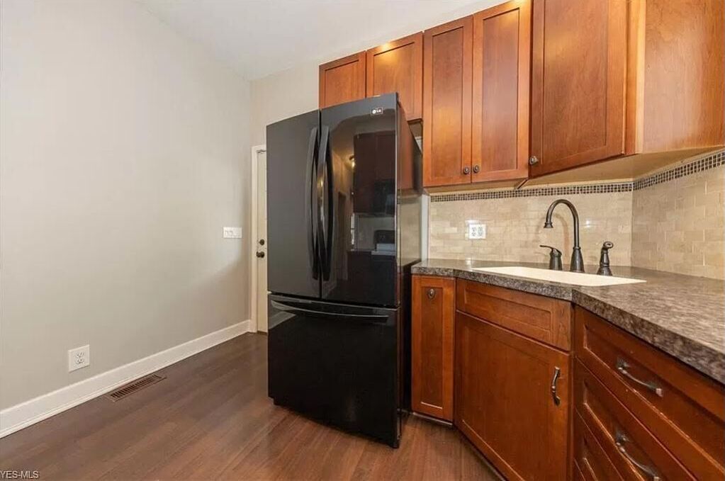 Una cocina con armarios de madera, un refrigerador negro, un lavamanos con grifo y salpicadero de azulejos.