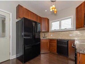 A kitchen with wooden cabinets, a black refrigerator, and a window with blinds. - Cozy 1-bedroom apartment in Cleveland's Little Italy! (Cleveland)