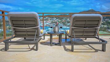 Two lounge chairs facing a pool with a city view, a small table with a bottle and glasses, and a metal grill structure.