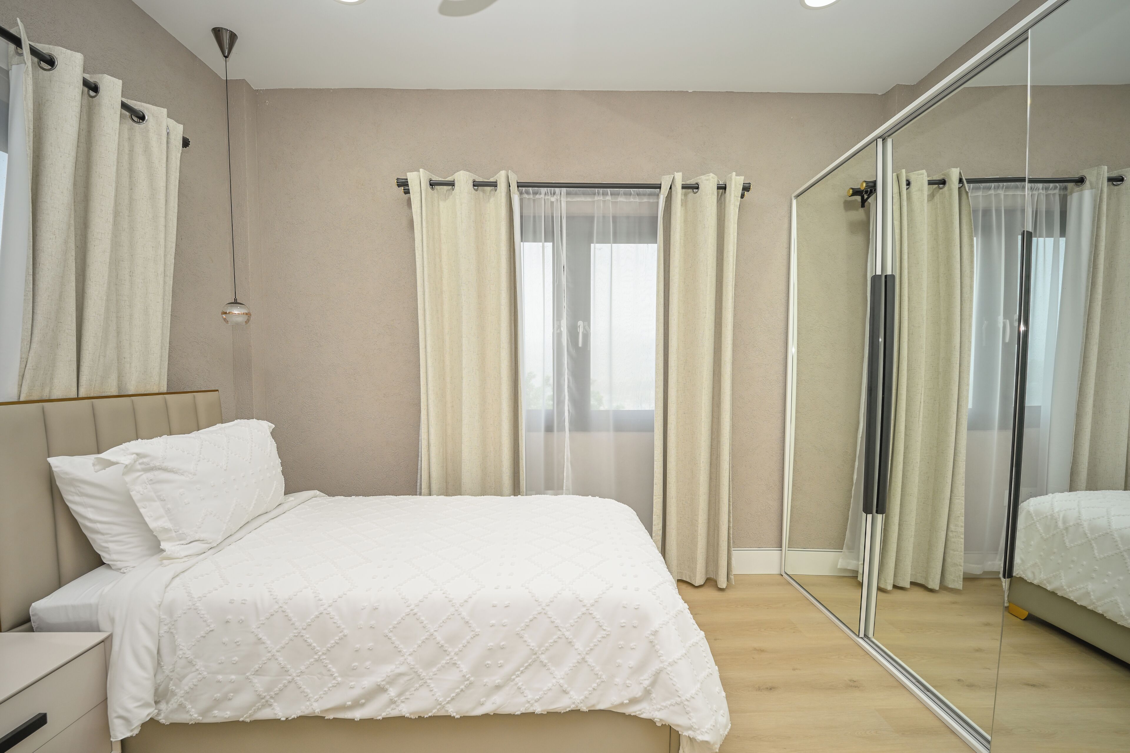 A bedroom with a bed, a nightstand, a mirror, and a window with curtains.