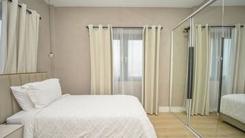A bedroom with a bed, a nightstand, a mirror, and a window with curtains.