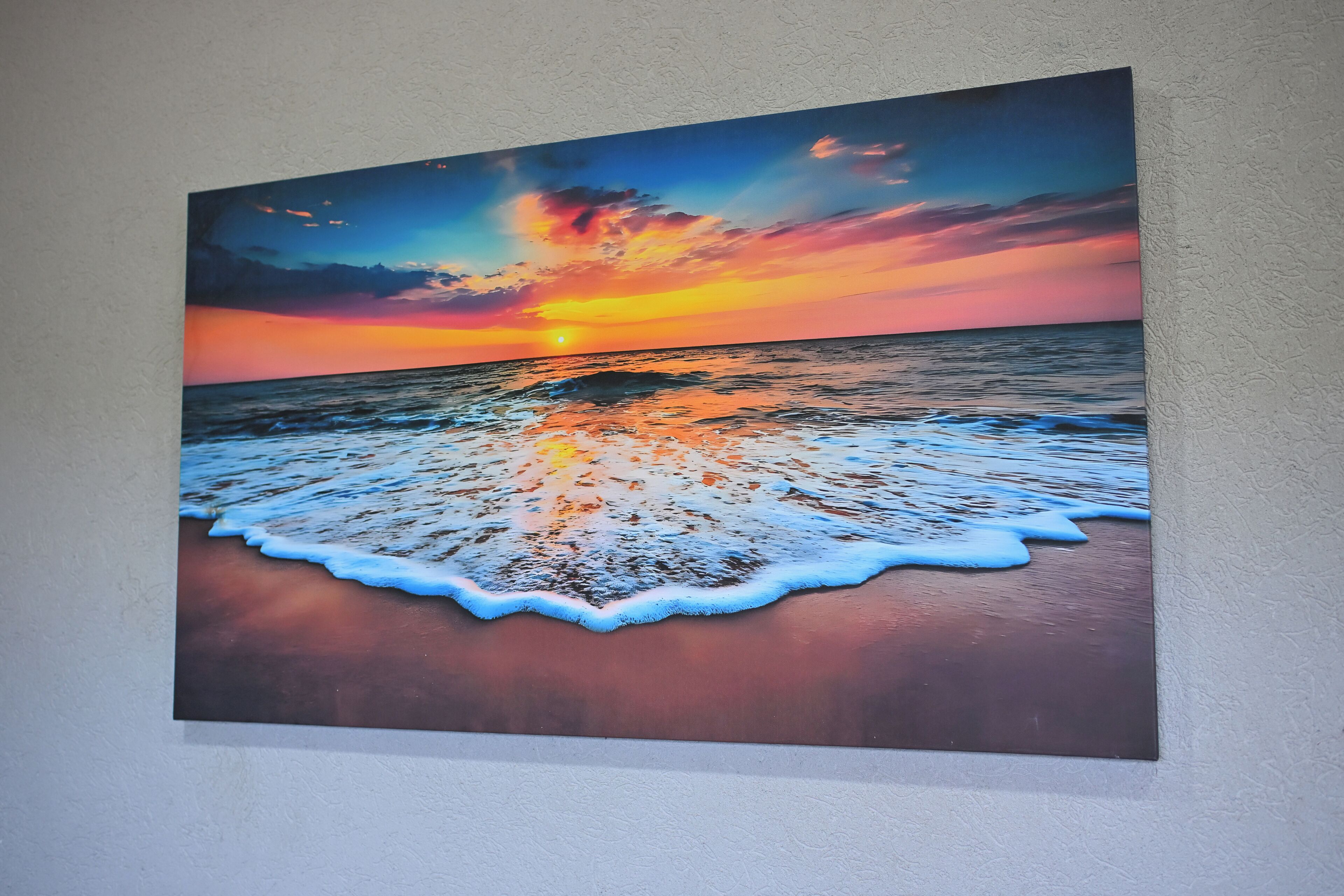 Un tableau représentant un coucher de soleil sur l’océan, avec des vagues sur la plage.